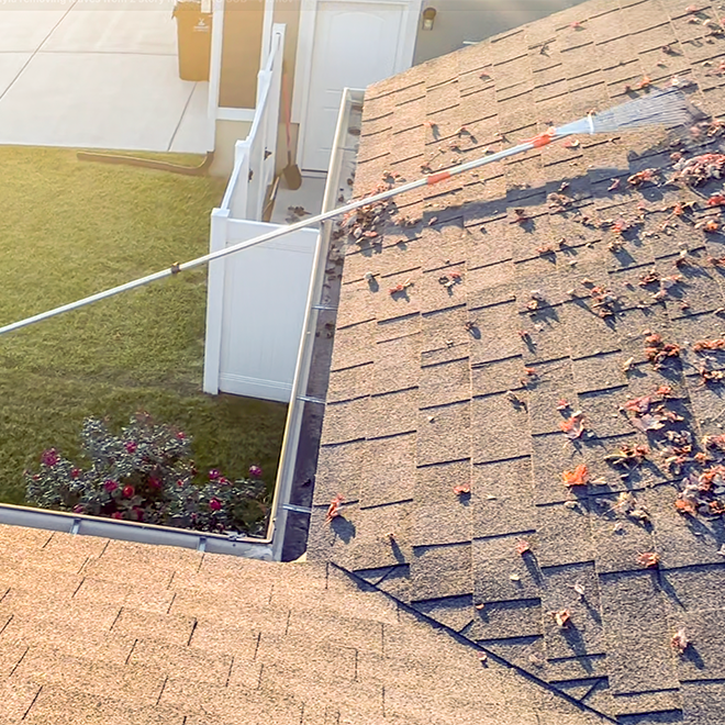 Roof cleaning process with a long-handled tool removing debris from a roof