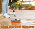 Extend-A-Reach telescoping extension pole with medium bristle scrub brush cleaning a wooden deck with soap and water. Perfect long-handle deck brush for exterior cleaning of patios, siding, gutters, and outdoor surfaces. Text on image reads: ‘Clean Your Deck With Ease.’